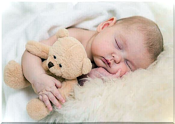 a little baby sleeps with a teddy bear in his armpit